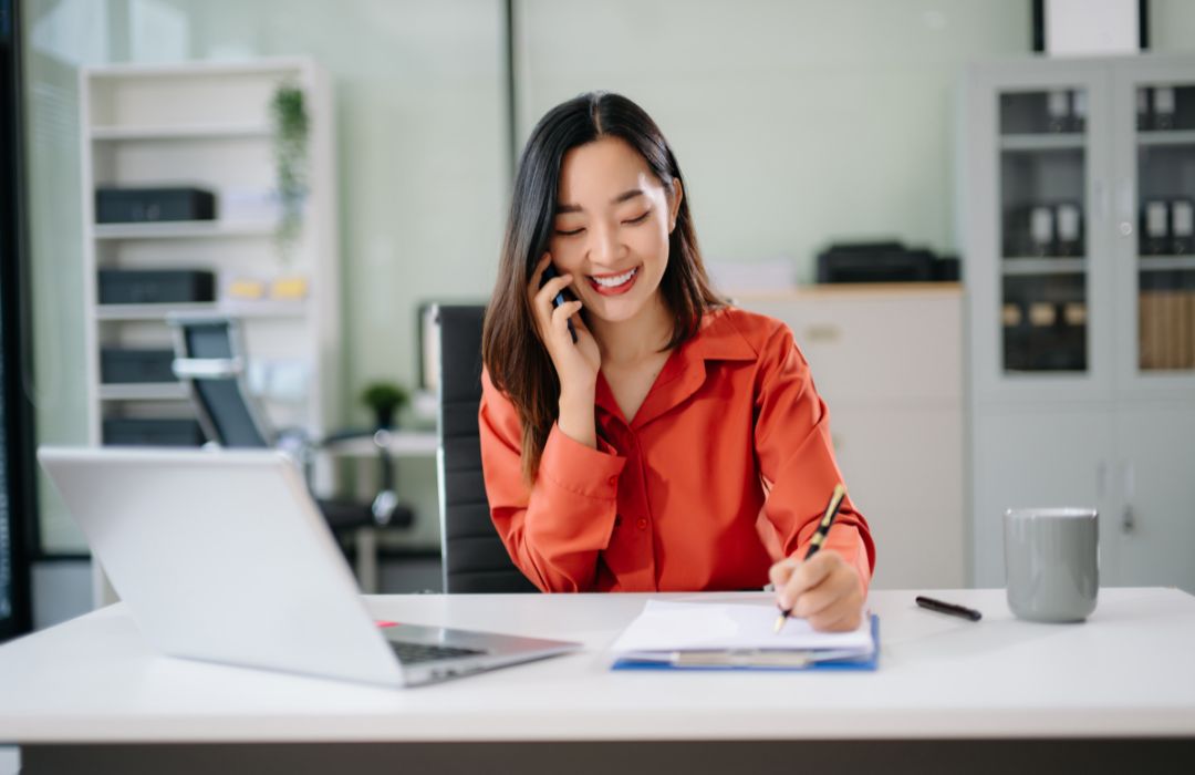 Office staff member taking a service call and writing notes for scheduling support