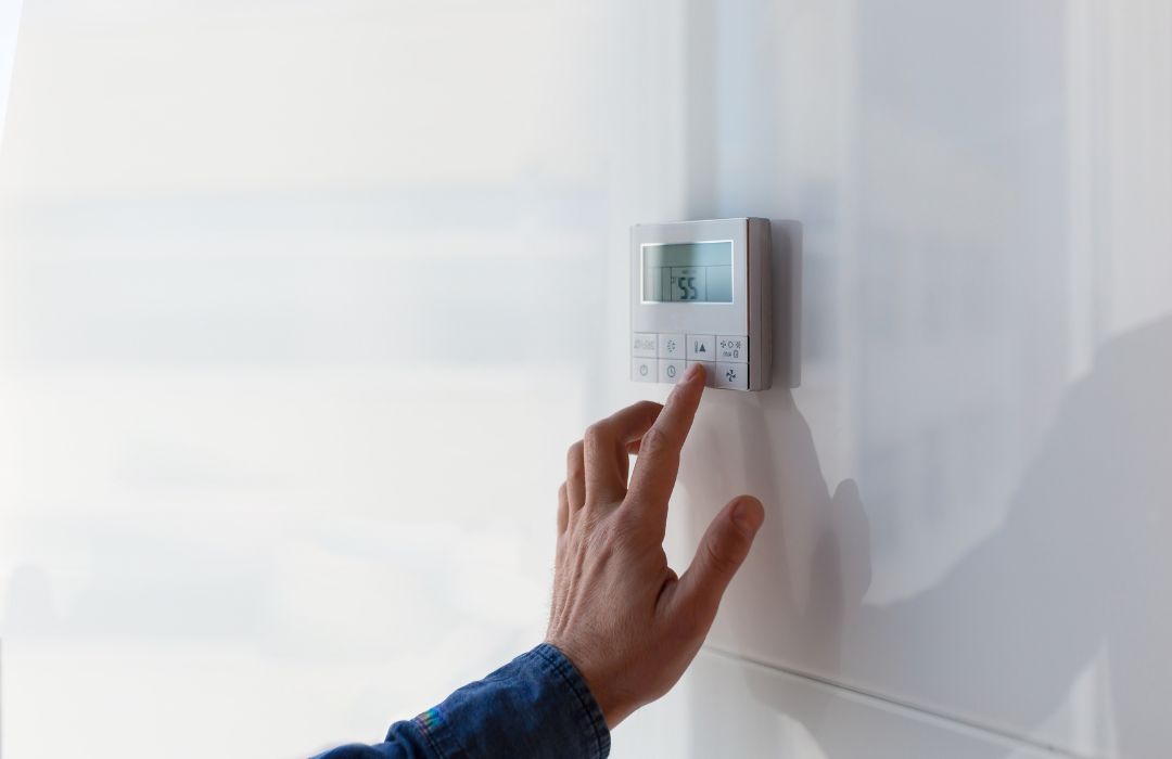 Tech adjusting a wall thermostat during residential HVAC maintenance and system performance checks